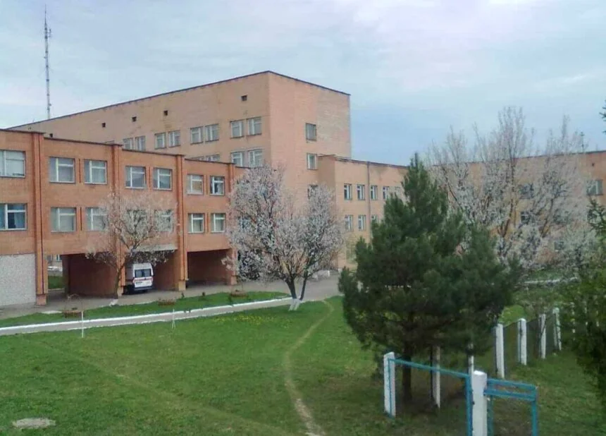 Цегляний корпус лікарні з аркою, швидкою допомогою та квітучими деревами