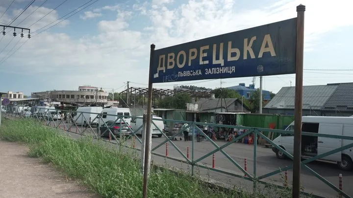 Синій вказівник зупинки Дворецька Львівської залізниці біля дороги й фургонів