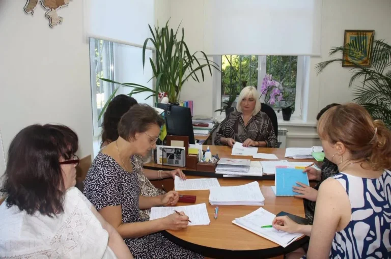 Жінки за круглим столом розглядають документи в кабінеті з гербом